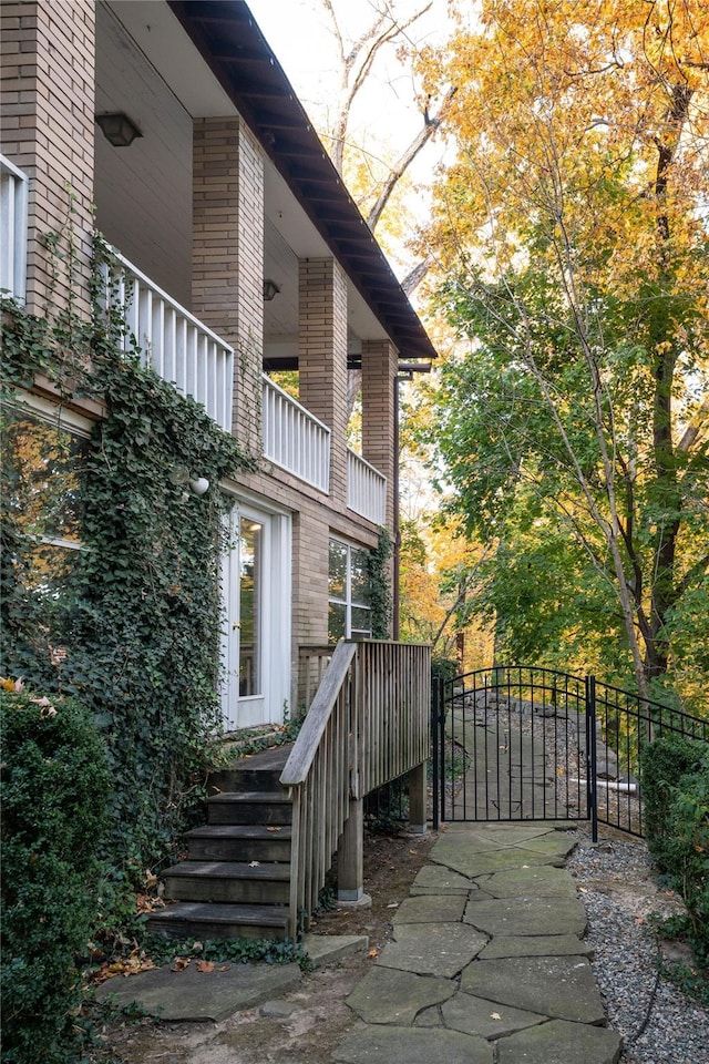 view of side of property with a gate, brick siding, fence, and a balcony