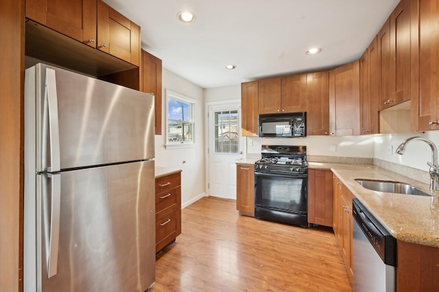 kitchen with black appliances, light stone counters, sink, and light hardwood / wood-style flooring