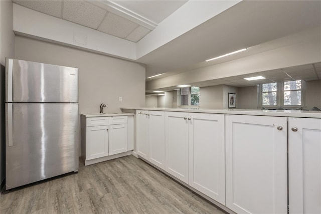 kitchen with a drop ceiling, sink, kitchen peninsula, stainless steel fridge, and white cabinets