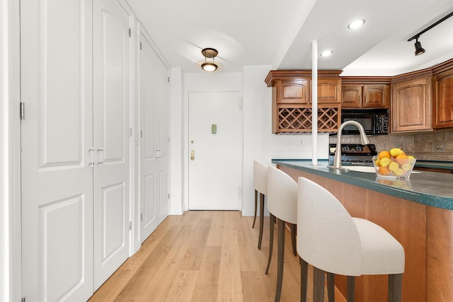 70-25 Yellowstone Blvd Unit 6O, Forest Hills, NY 11375 - kitchen with black microwave, dark countertops, decorative backsplash, light wood finished floors, and brown cabinets