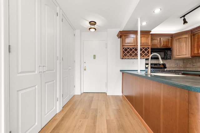 kitchen featuring sink, light wood-type flooring, backsplash, and stainless steel range oven