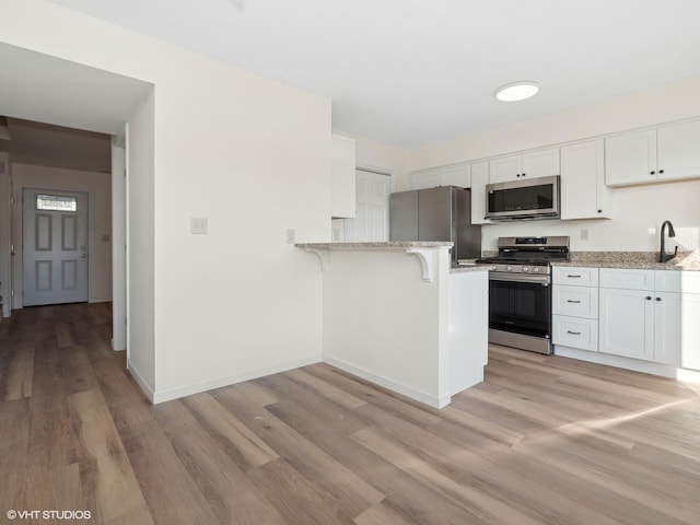 kitchen featuring white cabinets, light stone countertops, appliances with stainless steel finishes, and light hardwood / wood-style flooring