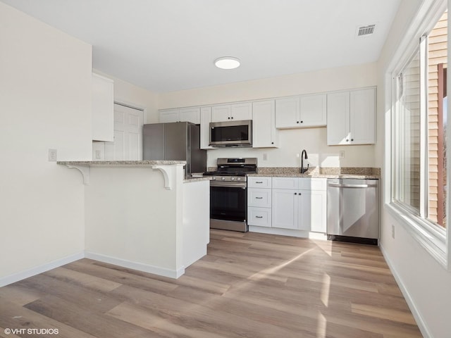 kitchen featuring kitchen peninsula, stainless steel appliances, white cabinetry, and light hardwood / wood-style floors