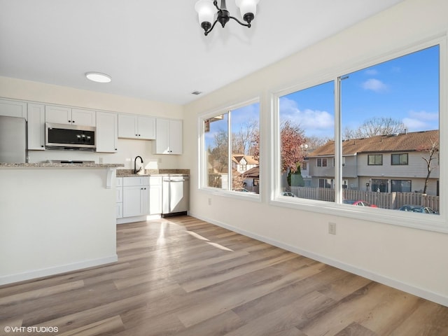 kitchen with an inviting chandelier, white cabinets, sink, light wood-type flooring, and stainless steel appliances