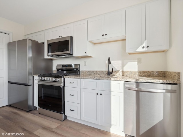 kitchen with light stone counters, white cabinets, light wood-type flooring, and appliances with stainless steel finishes