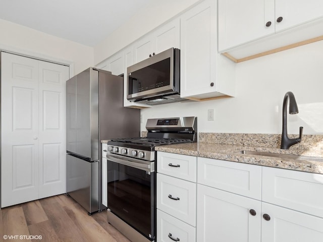 kitchen featuring sink, stainless steel appliances, light stone counters, light hardwood / wood-style flooring, and white cabinets