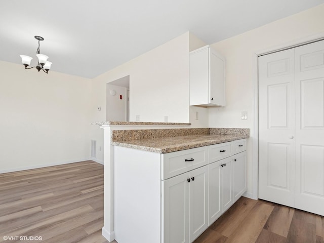 kitchen featuring kitchen peninsula, white cabinetry, light hardwood / wood-style flooring, and pendant lighting