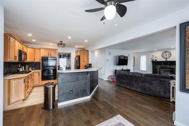 kitchen with hardwood / wood-style flooring, a tile fireplace, a center island, black appliances, and decorative backsplash