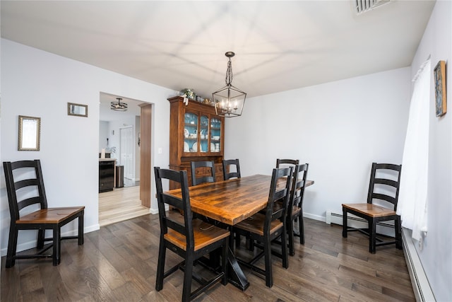 dining area featuring dark hardwood / wood-style flooring, a baseboard heating unit, and a notable chandelier