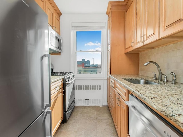 kitchen featuring radiator, light stone countertops, sink, stainless steel appliances, and decorative backsplash