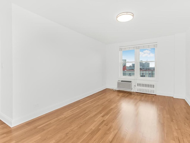 unfurnished room featuring a wall mounted air conditioner, radiator heating unit, and light wood-type flooring