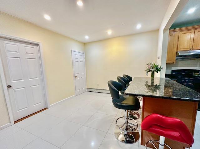 kitchen with a kitchen breakfast bar, a baseboard radiator, light tile patterned floors, and dark stone countertops