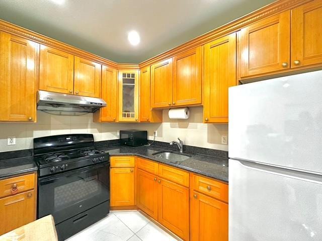 kitchen featuring dark stone counters, sink, white refrigerator, black gas stove, and light tile patterned flooring