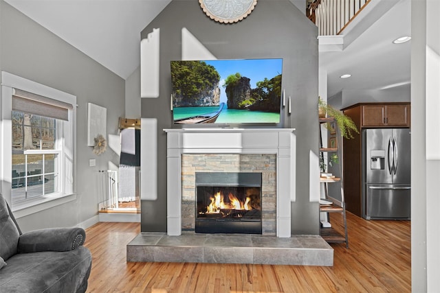 living room with a stone fireplace, lofted ceiling, and light hardwood / wood-style flooring