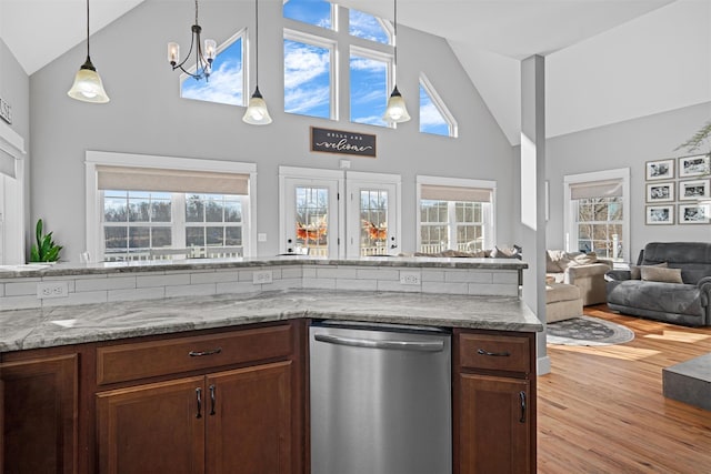 kitchen featuring light wood-type flooring, stainless steel dishwasher, light stone counters, high vaulted ceiling, and plenty of natural light