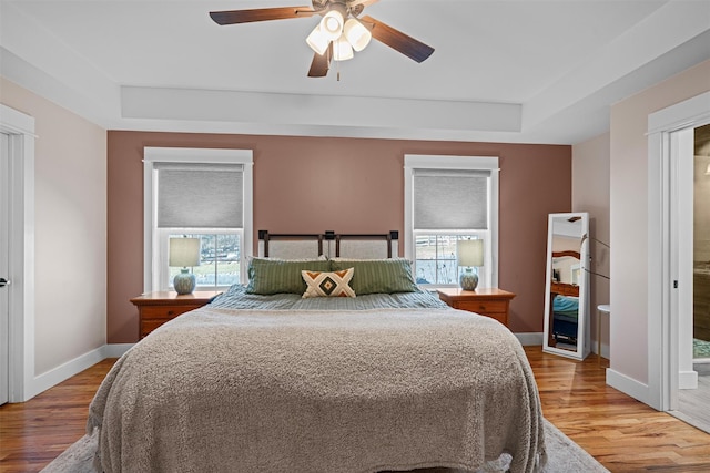 bedroom with a tray ceiling, multiple windows, ceiling fan, and hardwood / wood-style floors