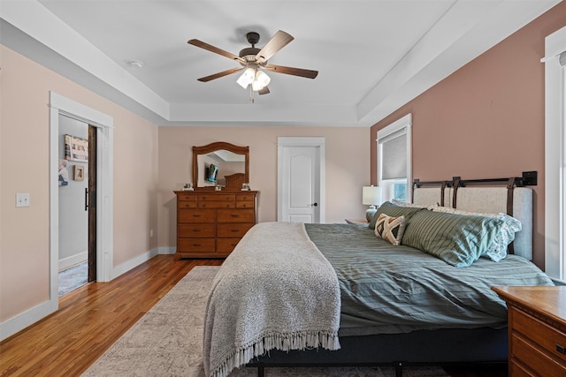 bedroom featuring a raised ceiling, ceiling fan, and light wood-type flooring