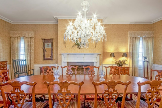 dining space featuring a fireplace, crown molding, an inviting chandelier, wainscoting, and wallpapered walls