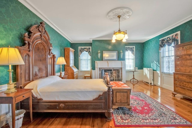 bedroom featuring wood finished floors, wallpapered walls, crown molding, and a premium fireplace