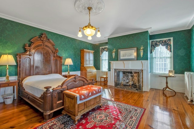 bedroom with a tile fireplace, a wainscoted wall, wallpapered walls, hardwood / wood-style floors, and crown molding