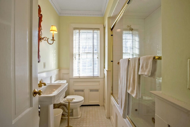 bathroom with a wainscoted wall, crown molding, bath / shower combo with glass door, a decorative wall, and toilet