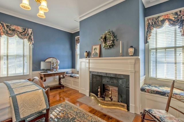 bedroom with a wainscoted wall, ornamental molding, wood finished floors, and a fireplace with flush hearth