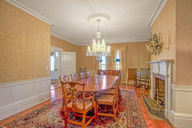 dining space with a wainscoted wall, ornamental molding, wood finished floors, and wallpapered walls