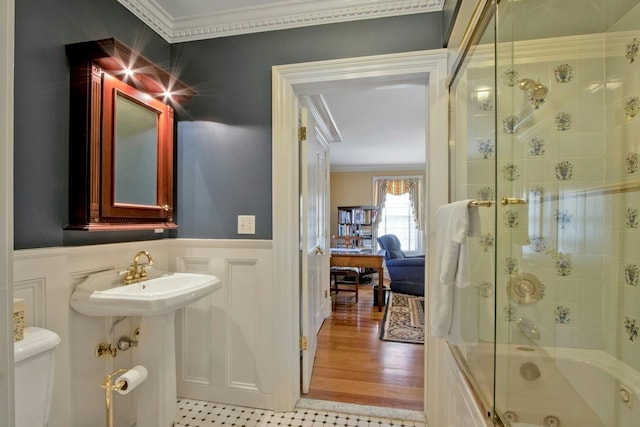 bathroom with a wainscoted wall, bath / shower combo with glass door, a decorative wall, toilet, and ornamental molding