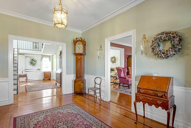 hall with a wainscoted wall, crown molding, wood finished floors, and an inviting chandelier