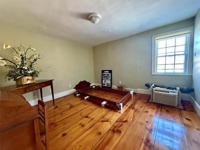 bedroom with wood-type flooring, baseboards, and an AC wall unit