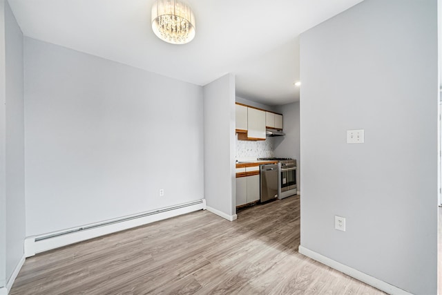 kitchen featuring backsplash, white cabinets, light wood-type flooring, a baseboard radiator, and stainless steel appliances