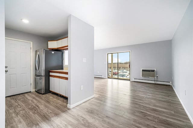 kitchen featuring stainless steel fridge, light wood-type flooring, baseboard heating, and a wall unit AC