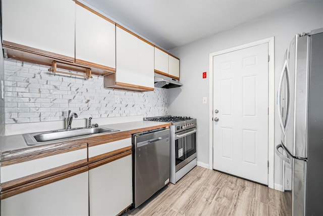 kitchen with decorative backsplash, appliances with stainless steel finishes, sink, white cabinets, and light hardwood / wood-style floors