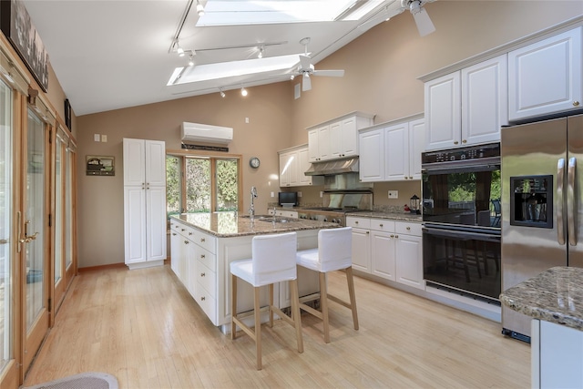 kitchen with a center island with sink, light hardwood / wood-style flooring, appliances with stainless steel finishes, light stone counters, and white cabinetry