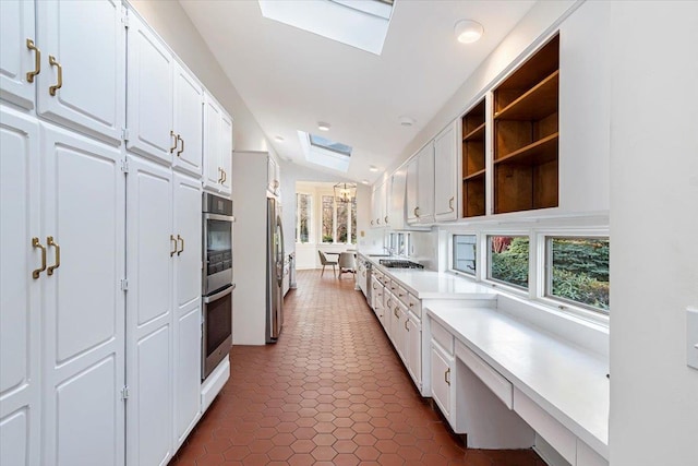 kitchen with white cabinets, dark tile patterned floors, lofted ceiling with skylight, and stainless steel appliances