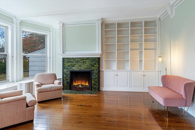 living area featuring a stone fireplace, ornamental molding, and hardwood / wood-style flooring