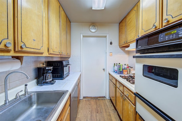 kitchen with tasteful backsplash, white appliances, sink, and light hardwood / wood-style flooring