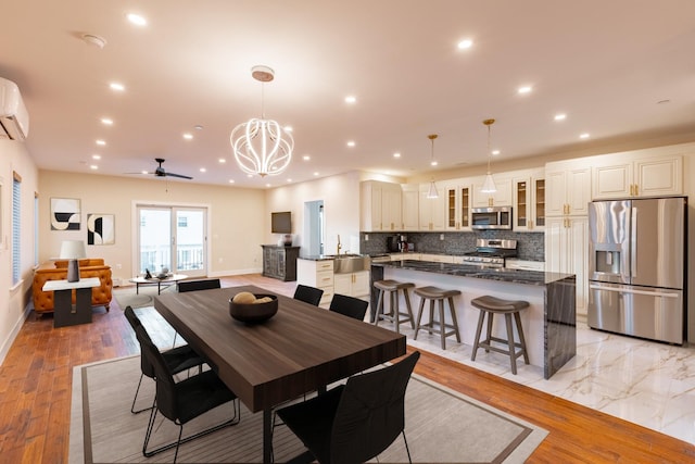 dining room with sink, a wall mounted air conditioner, light hardwood / wood-style floors, and ceiling fan with notable chandelier