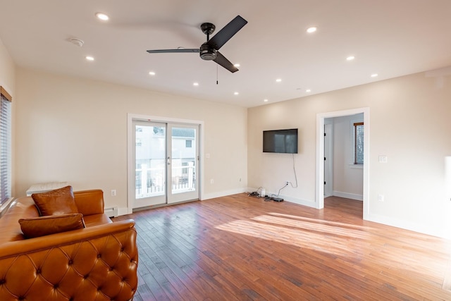 living room with ceiling fan, a baseboard heating unit, and light wood-type flooring