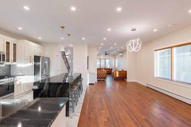 kitchen with stainless steel appliances, decorative light fixtures, dark stone countertops, white cabinets, and light hardwood / wood-style floors