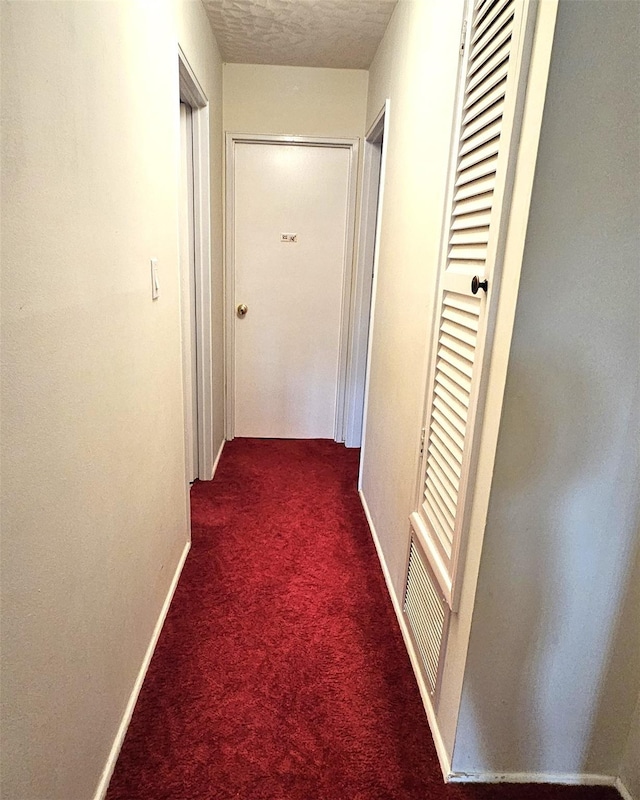 corridor with dark carpet and a textured ceiling