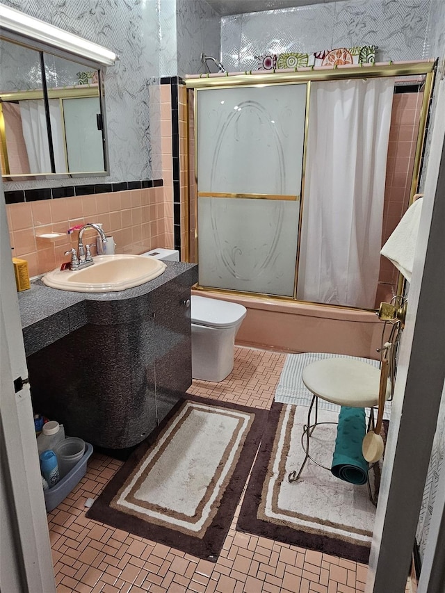 full bathroom with combined bath / shower with glass door, vanity, toilet, and tile walls