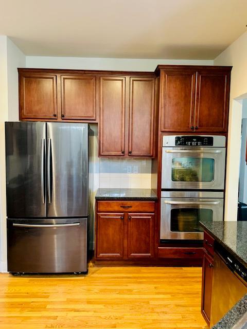 kitchen with appliances with stainless steel finishes, backsplash, light hardwood / wood-style flooring, and dark stone counters