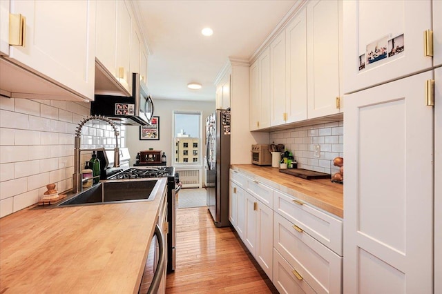 kitchen with wooden counters, white cabinets, stainless steel appliances, and light hardwood / wood-style floors