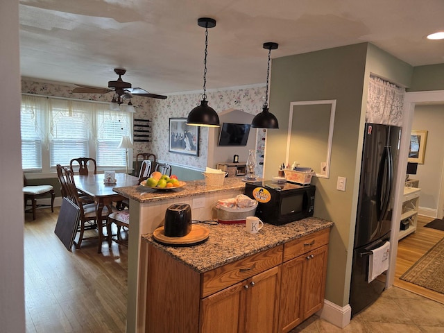 kitchen with light stone counters, ceiling fan, black appliances, light hardwood / wood-style floors, and hanging light fixtures