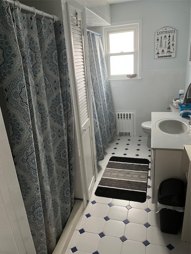 bathroom with radiator heating unit, walk in shower, toilet, vanity, and tile walls