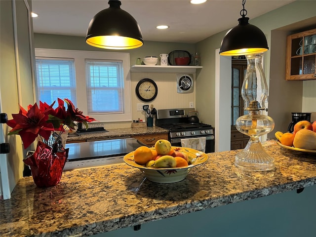 kitchen with stainless steel gas stove, kitchen peninsula, decorative light fixtures, and dark stone counters