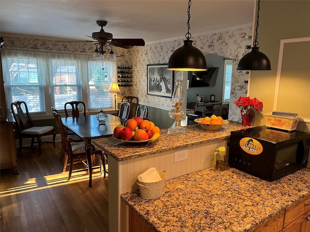 kitchen with light stone countertops, ornamental molding, ceiling fan, dark wood-type flooring, and hanging light fixtures