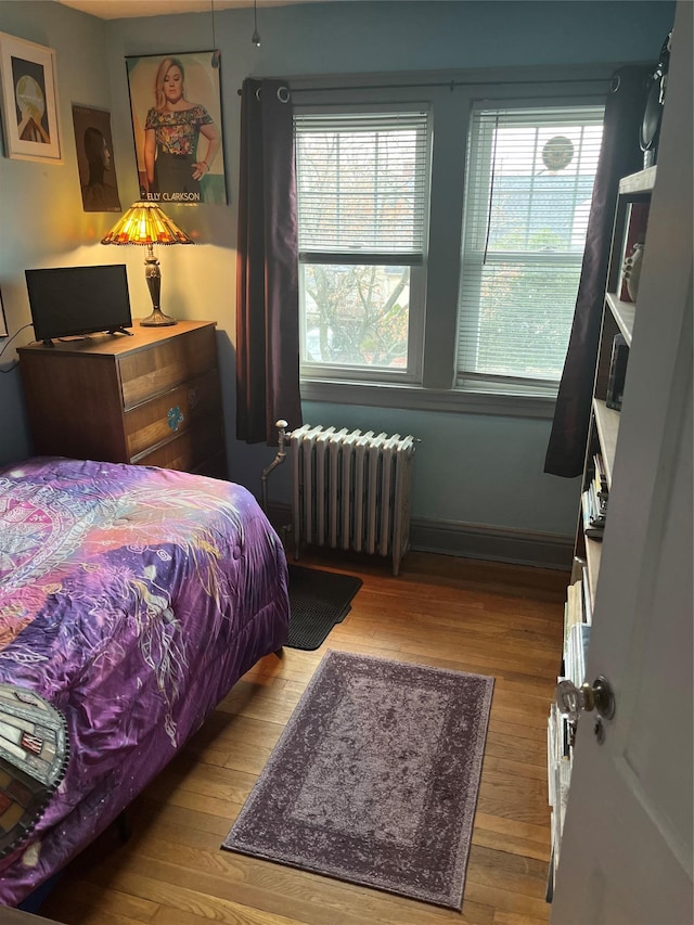 bedroom with radiator, wood-type flooring, and multiple windows