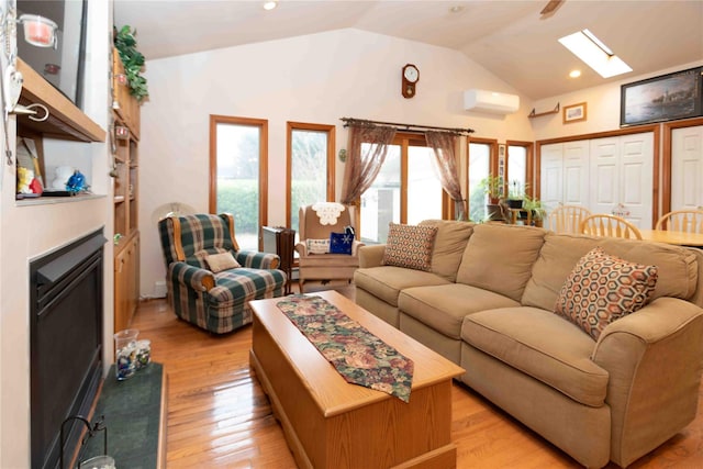 living room featuring a wall unit AC, vaulted ceiling with skylight, and light hardwood / wood-style floors